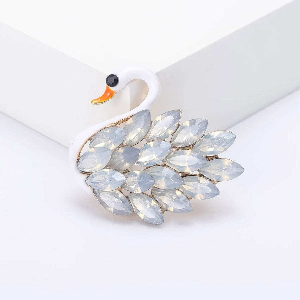 Swan brooch featuring smooth white body, faceted translucent stones, and orange beak, front view on white surface.
