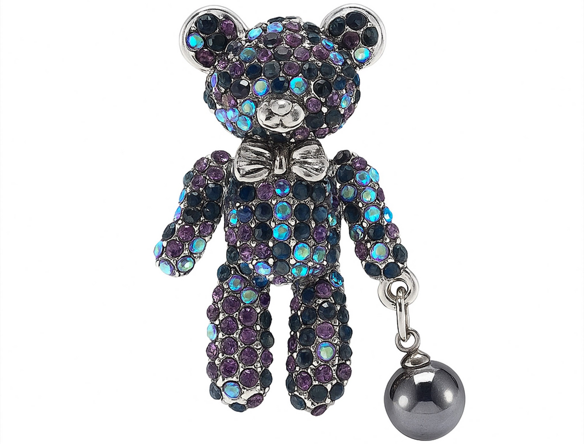 Teddy bear brooch with purple and blue iridescent stones, silver-tone bow, and dark metallic hanging faux pearl, cutout on white. Landscape crop for secondary use.