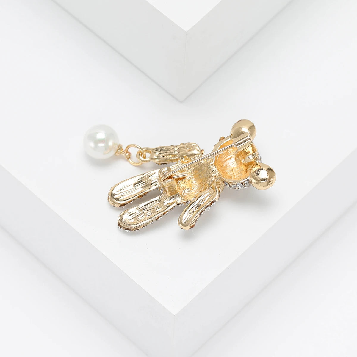 Reverse side of teddy bear brooch in textured gold-tone finish with attached white round bead, flat lay on white.