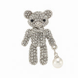 Teddy bear brooch with clear stones, silver-tone metal base and bow, and white round hanging bead, cutout on white background.