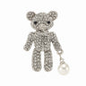 Teddy bear brooch with clear stones, silver-tone metal base and bow, and white round hanging bead, cutout on white background.