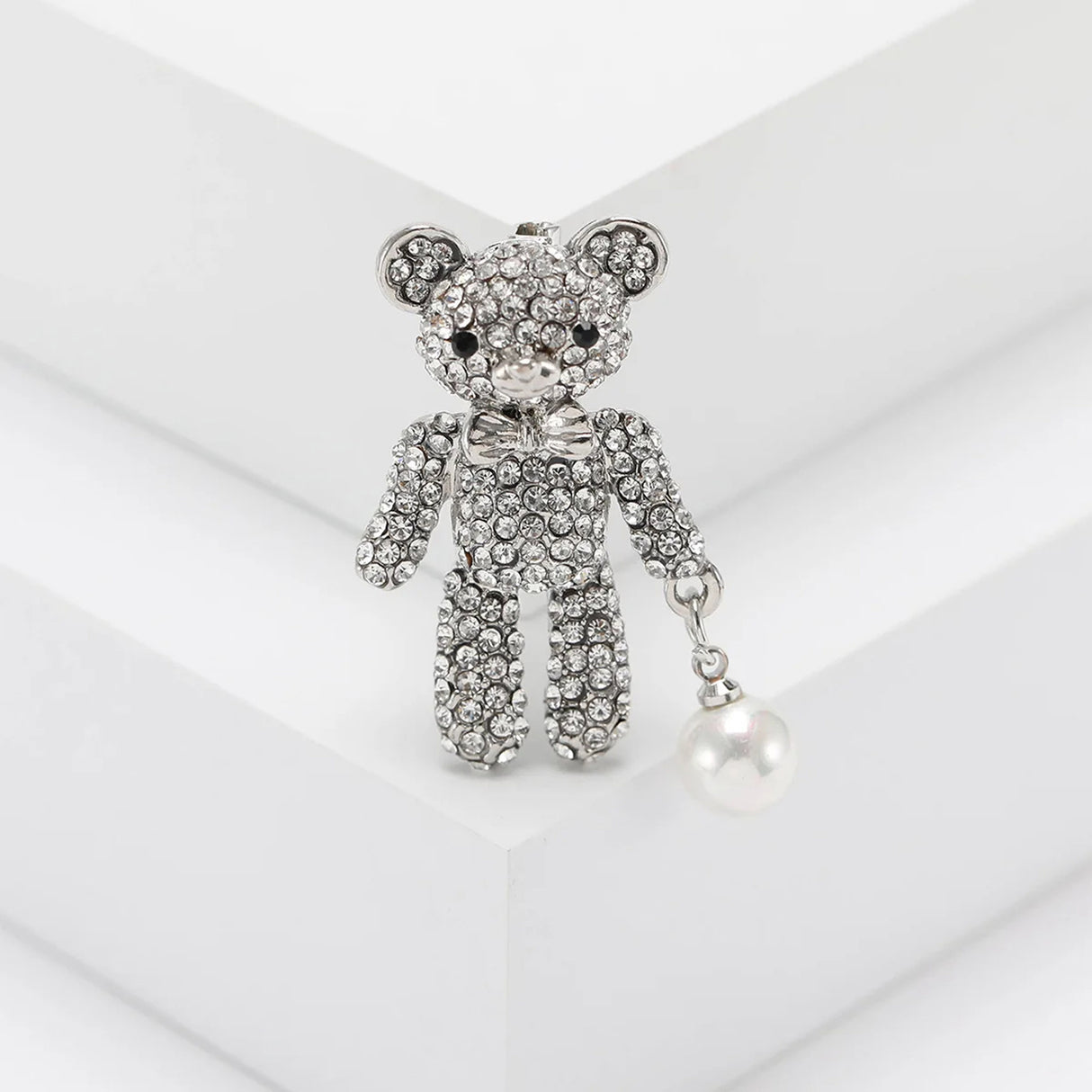  Teddy bear brooch with silver-tone metal, clear stones, and white round hanging faux pearl, upright pose on white display.