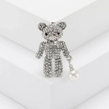  Teddy bear brooch with silver-tone metal, clear stones, and white round hanging faux pearl, upright pose on white display.