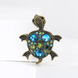 Antique-style turtle brooch with dotted gold-tone texture and clustered blue and green faceted stones, upright pose on white studio background.