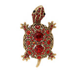 Tortoise brooch with gold-tone metal finish, red faceted center stones, and round red accents, cutout on white.