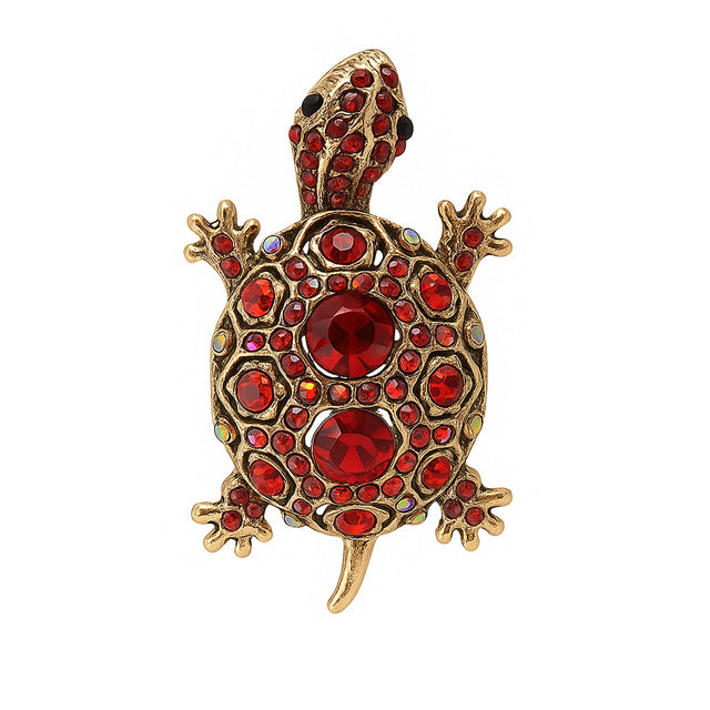 Tortoise brooch with gold-tone metal finish, red faceted center stones, and round red accents, cutout on white.