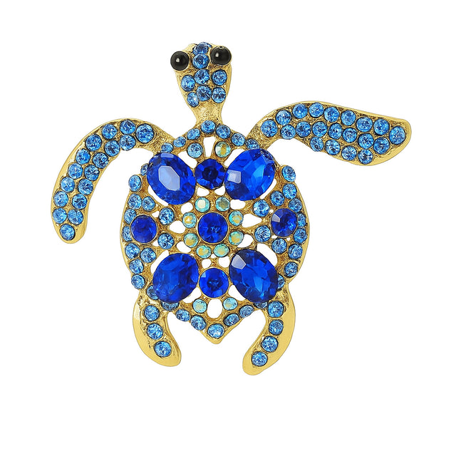 Sea turtle brooch in gold-tone metal base, with blue faceted center stones surrounded by small round accent crystals. Cutout on white background.